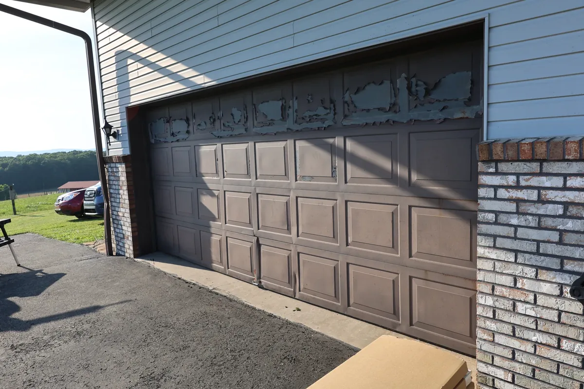 Woodgrain CHI on Brick garage before — A peeling, sun-blistered brown door on a brick and siding home.